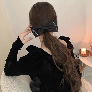 Detail of elegant black satin bow hair clip with pearl edges worn as a low ponytail accessory