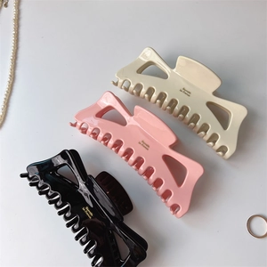 Three large acetate hair claws in cream, pink, and black colors with gold lettering