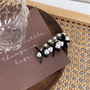 Detailed view of vintage pearl hair clip with black bows and gold metal base