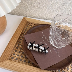 Close-up of pearl hair clip with black ribbon bow on vintage rattan background