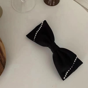 Elegant black velvet bow hair clip with white pearl details on a minimalist desk