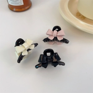 Detailed shot of small acrylic bow hair clips in cream white, light pink, and glossy black