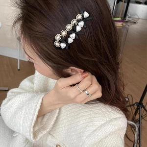 Vintage pearl hair clips with black bows and a green heart ring on a female model