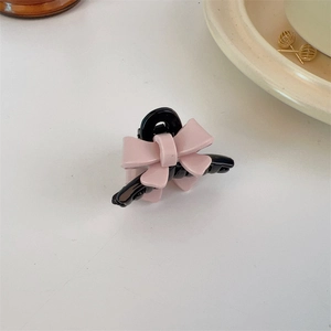 Detail view of a small black and pink bow hair claw clip on a clean white surface