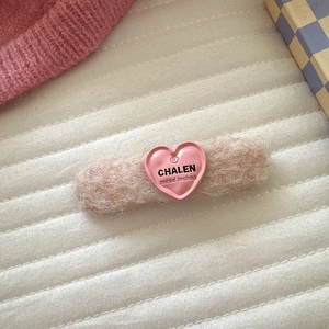 Detailaufnahme einer rosa Plüsch-Haarklammer mit einem herzförmigen Markenlogo-Detail