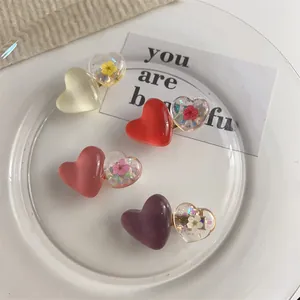 Détail de quatre pinces à cheveux coeur colorées avec fleurs séchées sur plat blanc