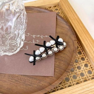 Vintage pearl hair clip with black bows and golden heart charms on aesthetic brown card