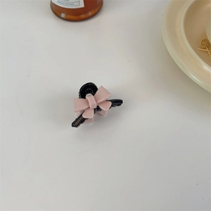 Detail view of pink acrylic bow hair claw clip on white surface with soft lighting