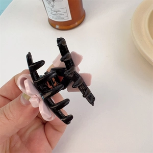 Detailed close-up of a black acrylic hair claw clip featuring a pink floral decoration