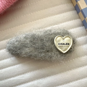 Nahaufnahme einer grauen Plüsch-Haarklammer mit Herzanhänger auf gestepptem Grund