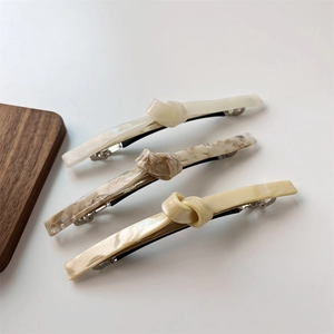Three-piece acetate twist knot hair clips in cream marble and pale yellow on a wood tray