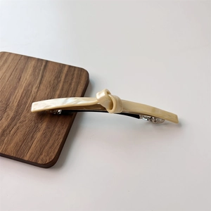 Close-up of a cream-colored twisted hair clip with marble texture on a wooden stand