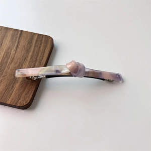Detail of twisted knot acetate hair clip with pink marble texture on wood surface