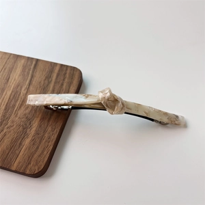 Detail of twist-knot spring hair clip with beige marble texture and silver metal base