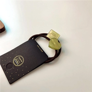 Detail of green acrylic heart and square charms on brown elastic hair tie packaging