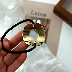 Détail de l'élastique à cheveux noir avec ornement rond en métal doré poli et creux