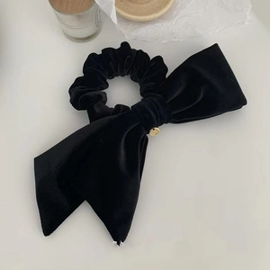 Detail of a black velvet hair scrunchie with a large bow and a small gold metal pendant
