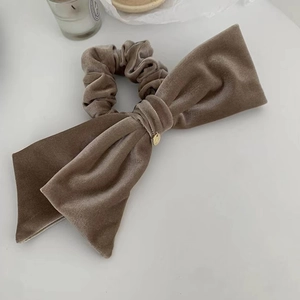 Detail of a large brown velvet bow scrunchie with a gold pendant on a white table