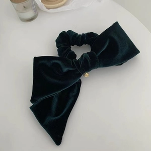 Detailed close-up of dark green velvet bow hair scrunchie with a small gold metal tag