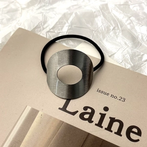 Gros plan sur un élastique à cheveux avec un pendentif circulaire en métal brossé gris foncé