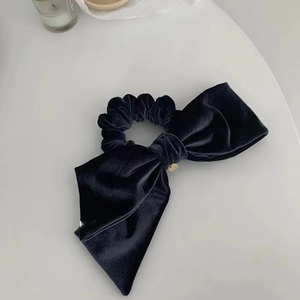 Detail of dark blue velvet bow hair tie with a round golden metallic pendant charm
