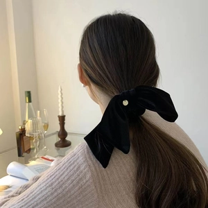 Detail view of a large black velvet bow hair scrunchie styled in a low ponytail