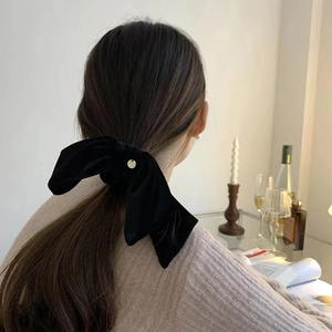 Elegant black velvet bow hair scrunchie with a gold pendant worn in a low ponytail