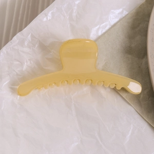 Gros plan d'une pince à cheveux en résine jaune pâle aux dents lisses sur papier