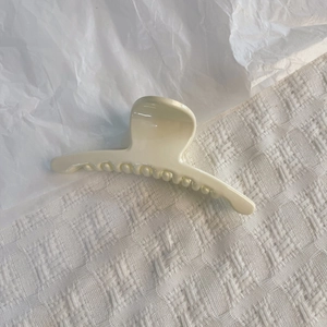 Gros plan d'une pince à cheveux crème sur un tissu texturé blanc avec un style minimaliste