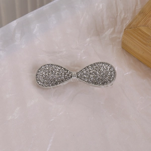 Détail de la pince à cheveux nœud argenté ornée de strass brillants sur fond texturé blanc