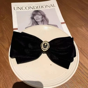Detail of a black velvet bow hair clip with a gold-rimmed rose pearl on a white ceramic plate