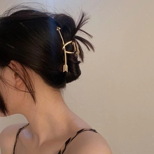 Elegant gold metal arrow shaped hair claw clip for women shown on a stylish bun hairstyle
