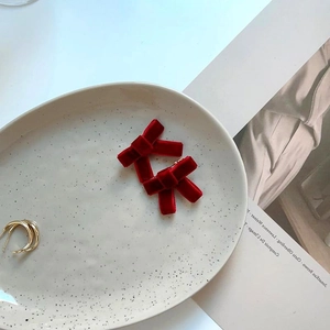 Elegantes Paar rote Samt-Schleifenspangen und mehrlagiger goldener Metallring auf Keramiktablett