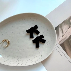 Elegante schwarze Samtbogen-Haarspangen und goldene Creolen auf einem Keramiktablett