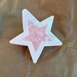 Dettaglio della molletta a stella in acetato con texture marmorizzata rosa e scritte dorate