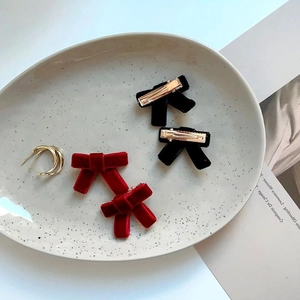 Elegante Haarklammern aus rotem und schwarzem Samt mit goldpolierten Creolen auf Keramiktablett