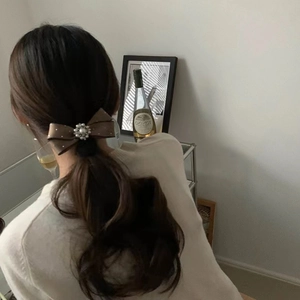 Detail of a brown silk bow hair clip with pearl center on dark hair ponytail