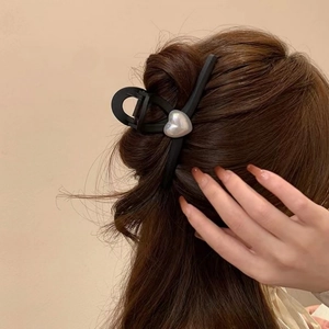 Detail view of a matte black hair claw clip with a heart-shaped pearl on dark brown hair