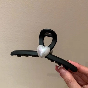Detailed view of large matte black claw clip with iridescent heart-shaped pearl ornament