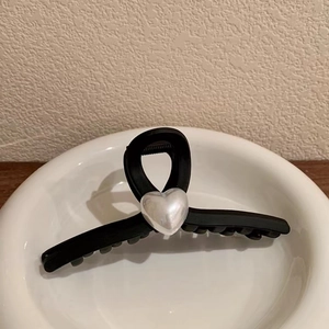 Close-up of matte black hair claw with pearl heart inlay displayed on a ceramic dish