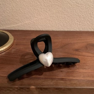 Detailed view of matte black hair claw clip featuring a centered white heart pearl accent