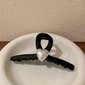 Matte black heart hair claw clip with pearl center decoration in a white ceramic bowl