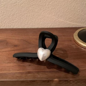 Matte black heart-shaped hair claw clip with pearl-like finish on a wooden surface