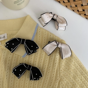 Close-up of black and cream bow hair clips with white pearls on a soft knit fabric