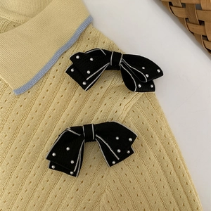 Detailed view of black bow hair clips with white pearls on a yellow knit cardigan