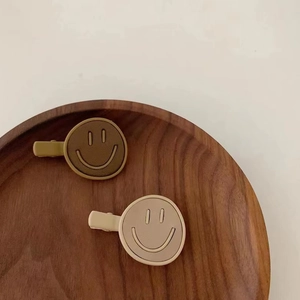 Close-up of leather smiley face hair clips in beige and brown on a wooden tray