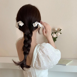 Detail of white bow hair clips with black trim and pearl accents on braided hair