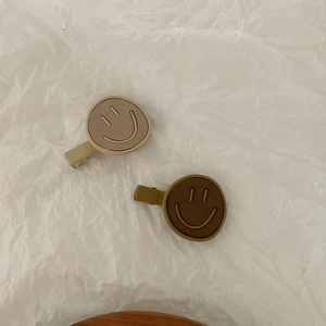 Detail view of khaki and brown smiley face hair clips on textured white paper background