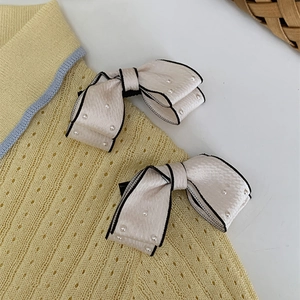Detail of elegant cream bow hair clips with black edging and pearls on knit fabric