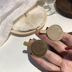 Detail of leather smiley face duckbill hair clips in khaki and dark brown colors